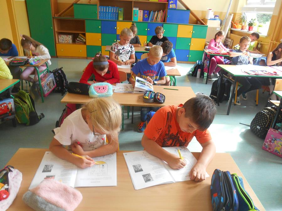 Dzieci z Łękawicy siedzą w ławkach w klasie i wypełniają ćwiczenia do lekcji regionalizmu.