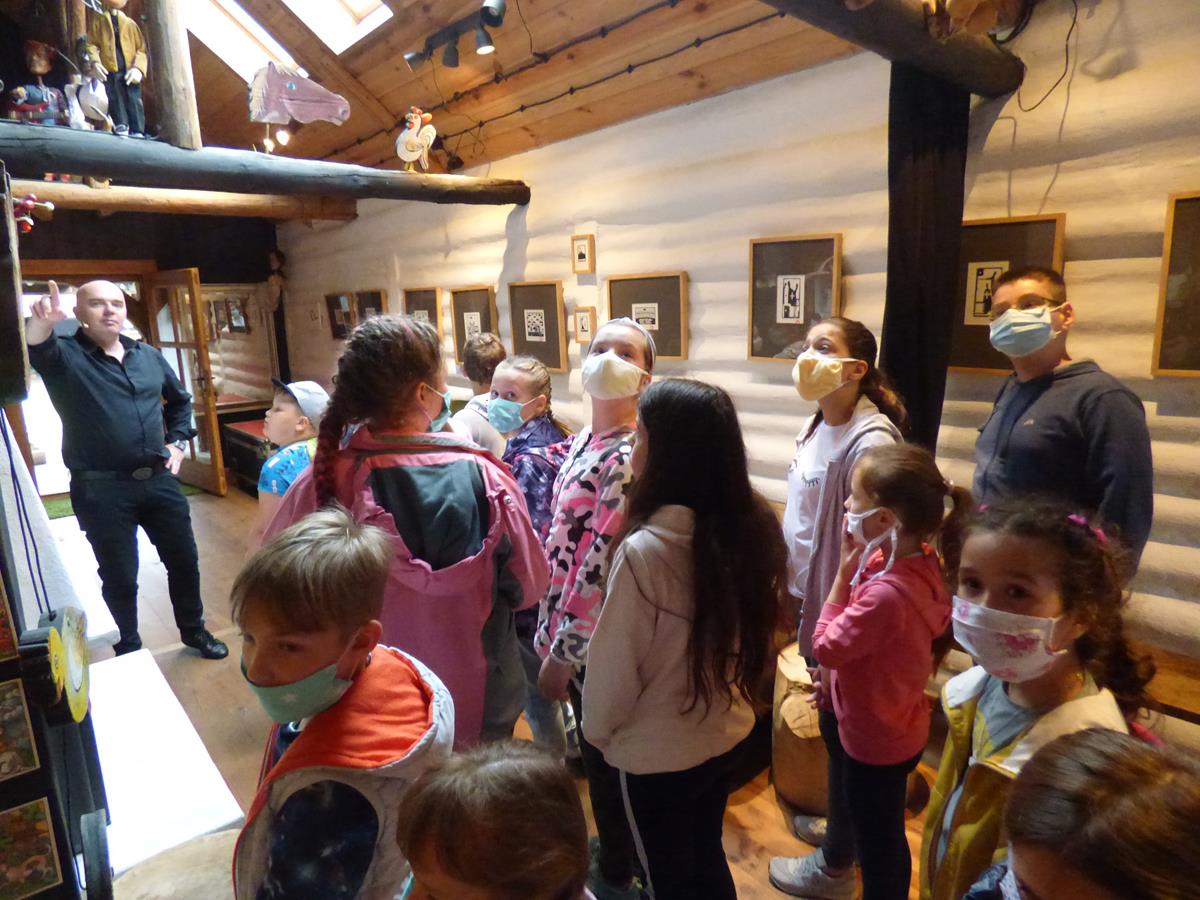 Dzieci znajdują się w budynku Zaułku Animacji i stojąc oglądają różnego rodzaju kukiełki.