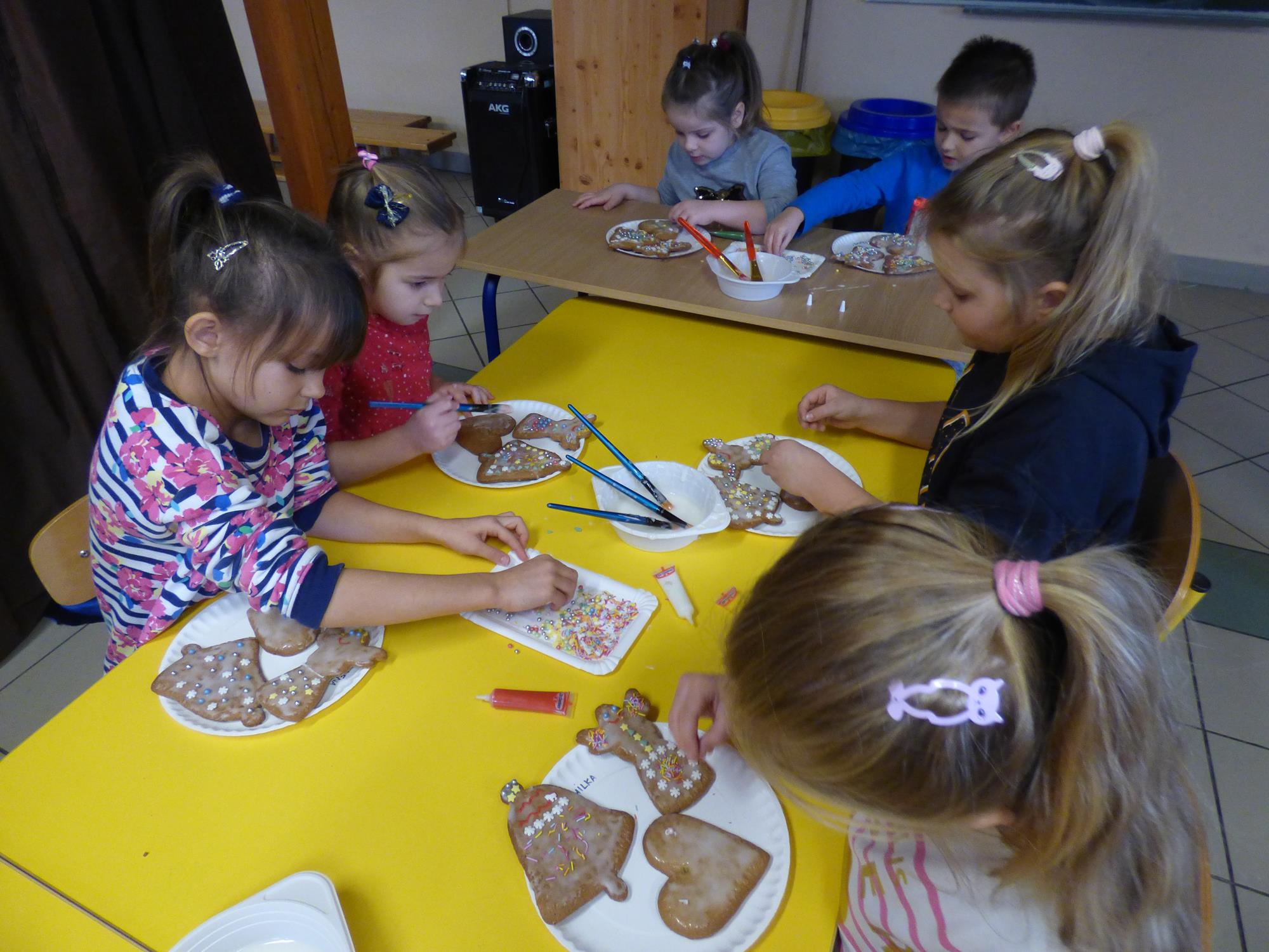 Dzieci z grupy Starszaków dekorują pierniczki siedząc przy stole.