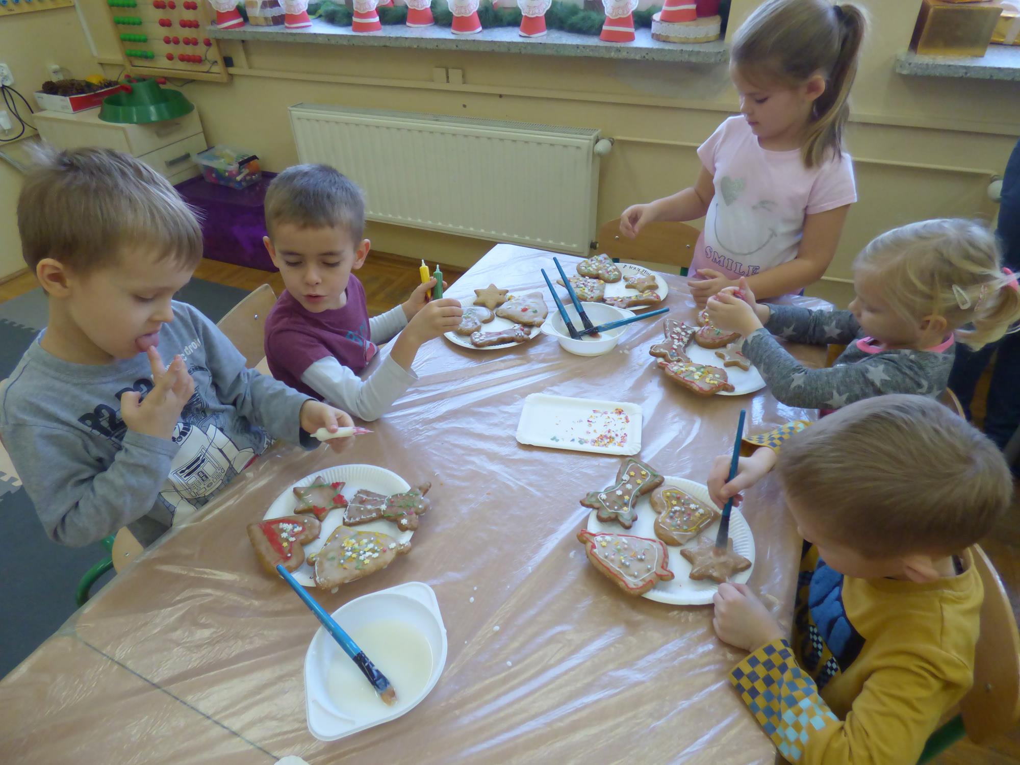 Przedszkolaki siedzą przy stoliku i dekorują świąteczne pierniczki.