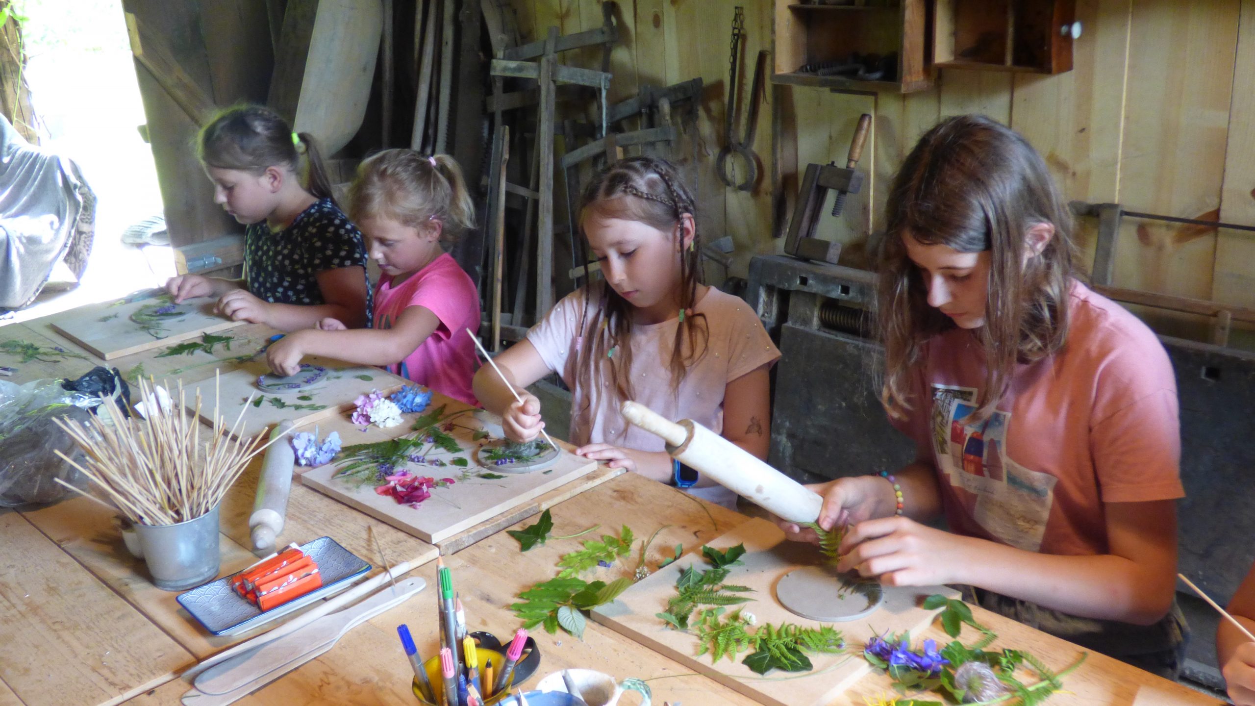 Zdjęcie przedstawia uczestników wyjazdu, znajdujących się w pracowni artystycznej. Tworzą oni własne medaliony z żywych kwiatów oraz liści.