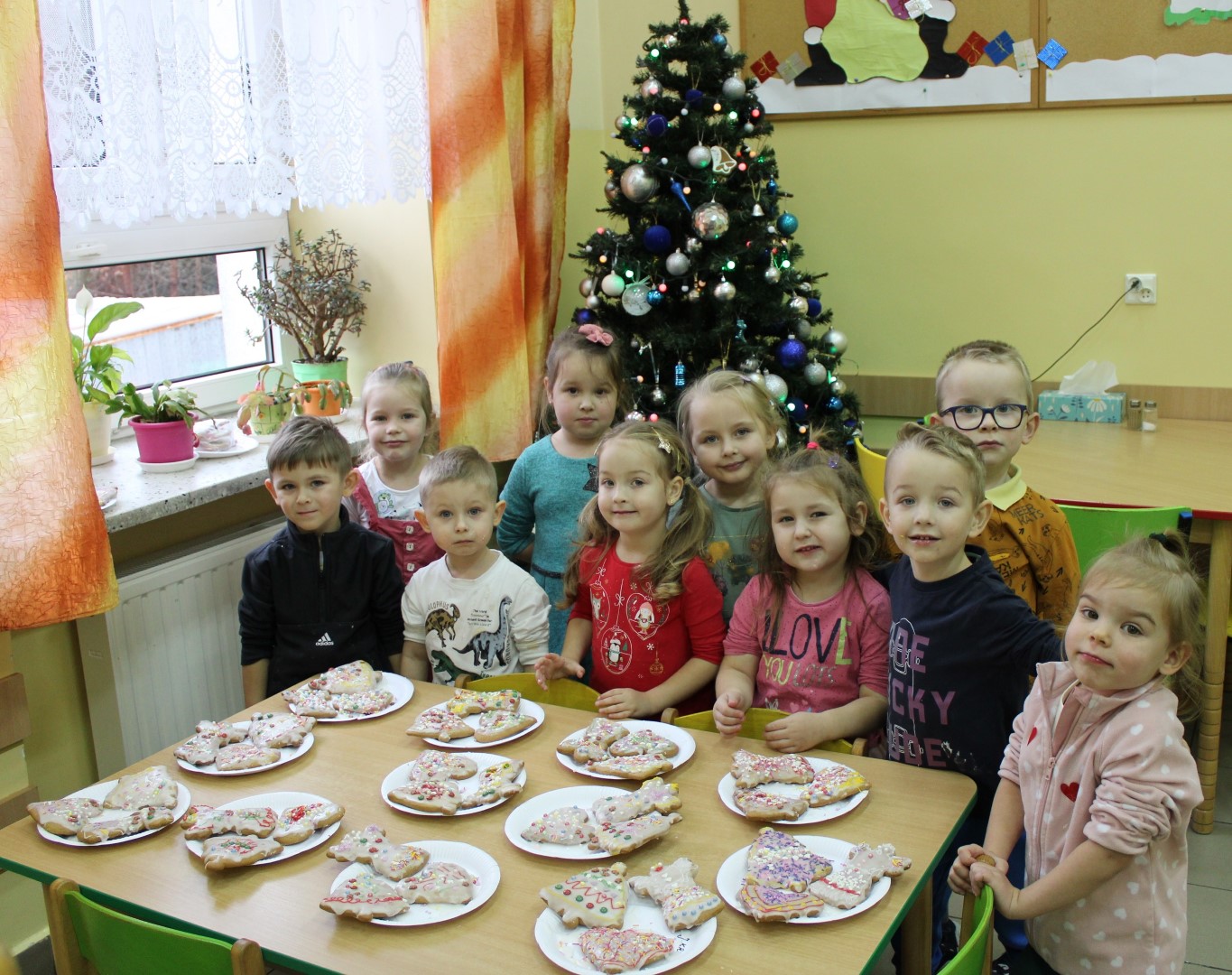Grupa przedszkolaków ze Stryszowa stoi za stołem, na którym zostały poukładane udekorowane pierniczki.