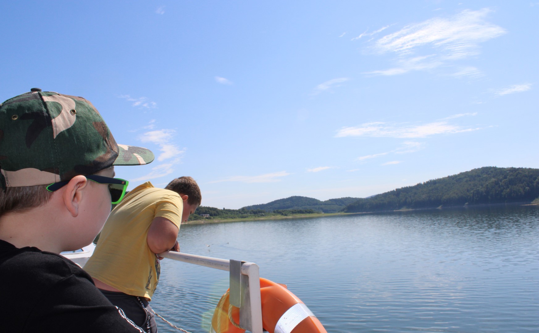 Zdjęcie przedstawia dwóch chłopców podczas rejsu statkiem po Jeziorze Mucharskim, wyglądają oni przez burtę, spoglądając na wodę.