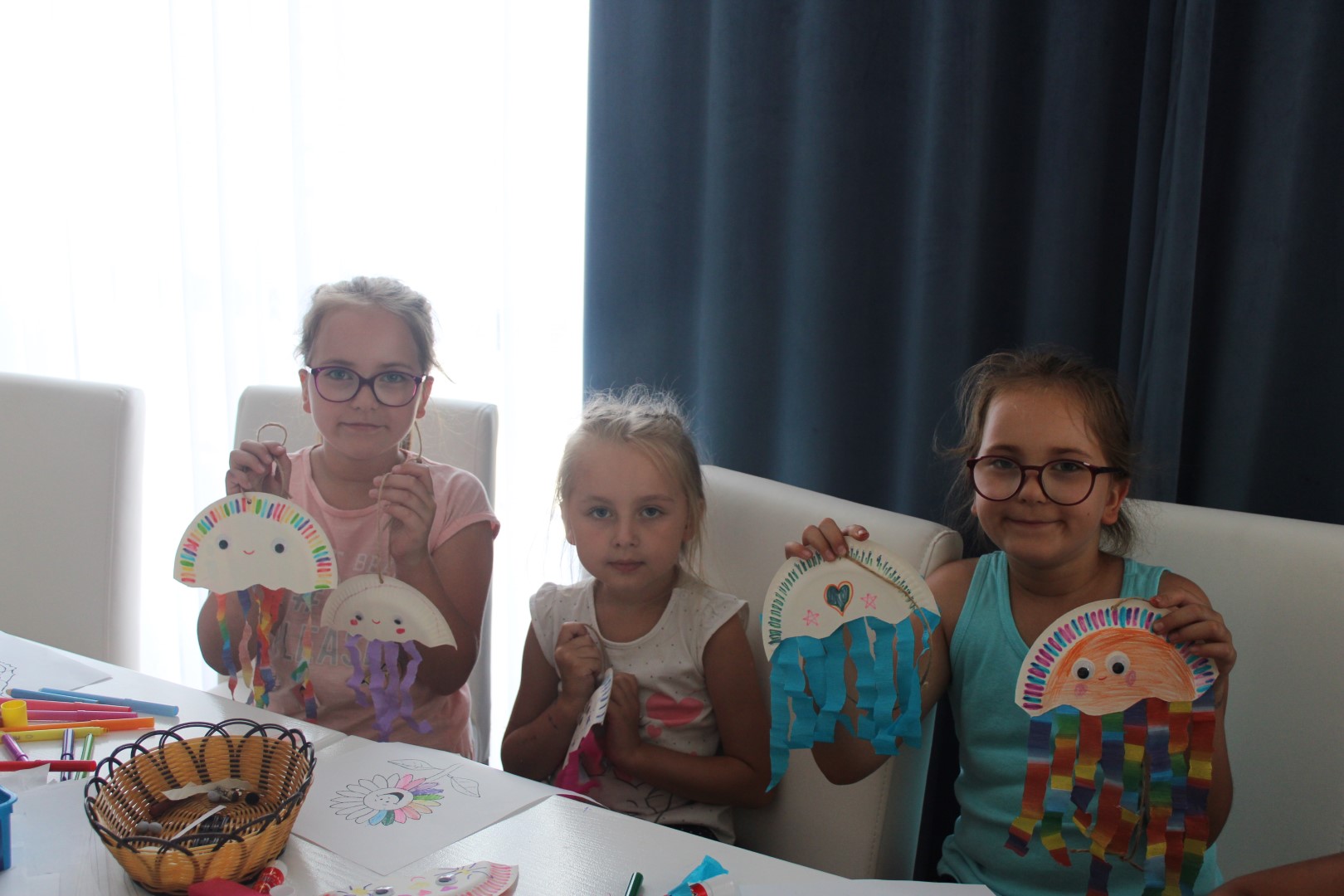 Zdjęcie przedstawia trzy dziewczynki podczas wakacyjnych zajęć plastycznych. Pozują do zdjęcia z wakacyjnymi, kolorowymi meduzami.