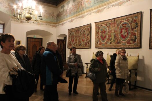 Zdjęcie przedstawia uczestników wycieczki do Zamku Królewskiego na Wawelu, którzy słuchają przewodnika oprowadzającego ich po Reprezentacyjnych Apartamentach Królewskich.