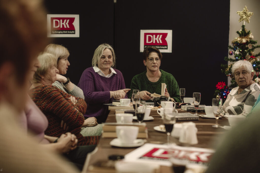 Grupa kobiet przy stole, w tle logo DKK - dyskusyjnego klubu książki