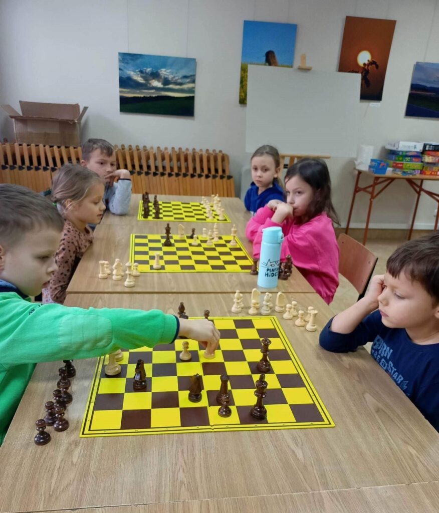 Na zdjęciu znajduje się sześcioro dzieci, które siedzą przy stolikach i rozgrywają partię szachów podczas Turnieju Szachowego organizowanego przez Gminny Ośrodek Kultury w Stryszowie podczas Ferii zimowych.