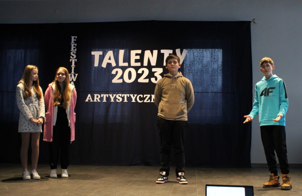 Na zdjęciu znajdują się dwie dziewczynki i dwóch chłopców ze Szkoły Podstawowej im. Janusza Korczaka w Dąbrówce, którzy występują na scenie podczas Międzyszkolnego Talent Show organizowanego przez Gminny Ośrodek Kultury w Stryszowie w Domu Strażaka w Łękawicy.