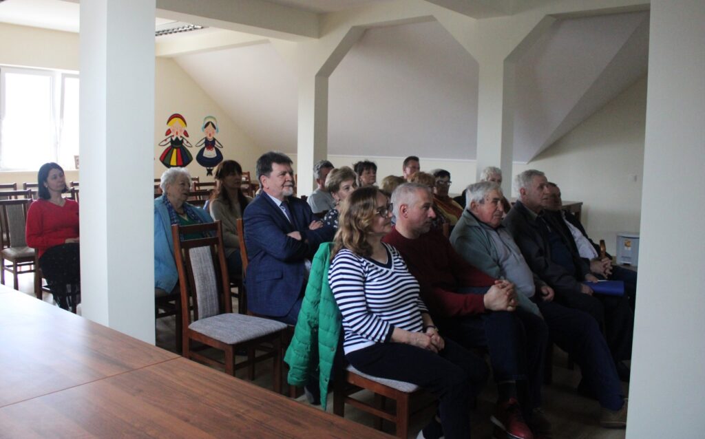 Zdjęcie przedstawia dziewiętnaście osób, siedzących na krzesłach w świetlicy Koła Gospodyń Wiejskich w Łękawicy na wykładzie „Funkcjonowanie Gromady Chłopskiej w galicyjskiej Łękawicy”.