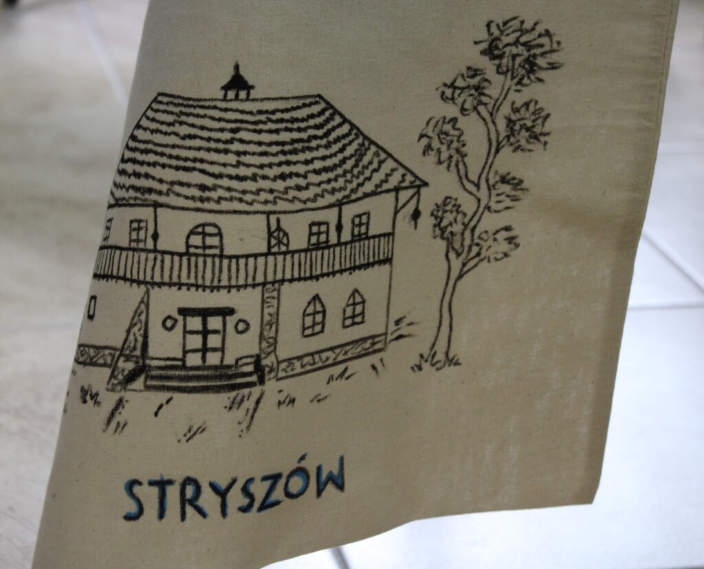Zdjęcie przedstawia wiszącą płócienną torbę, na której namalowany jest Dwór w Stryszowie.