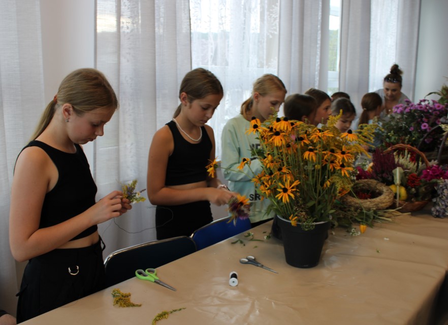 Na zdjęciu znajduje się młodzież, która wije wianki z polnych kwiatów podczas Stryszowskiego Święta Plonów z Megitzą.