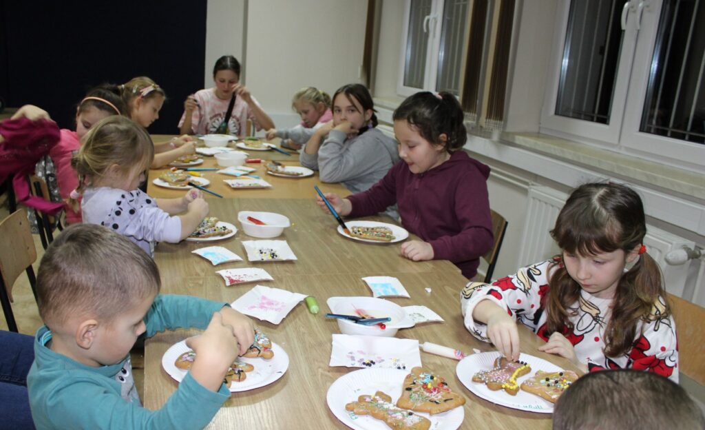 W świetlicy Gminnego Ośrodka Kultury w Stroniu dzieci siedzą przy stole i dekorują pierniczki.