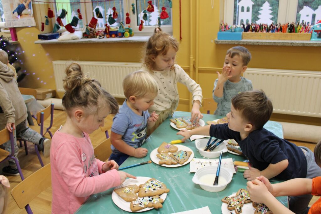 Przedszkolaki z Łękawicy siedzą przy stole i oblizując palce próbują smak lukru, którym pomalowały pierniczki.