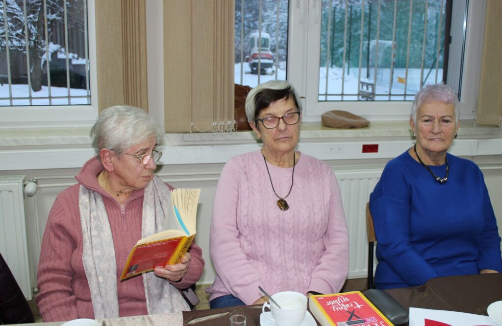 Trzy kobiety siedzą przy stole. jedna trzyma książkę w dłoni