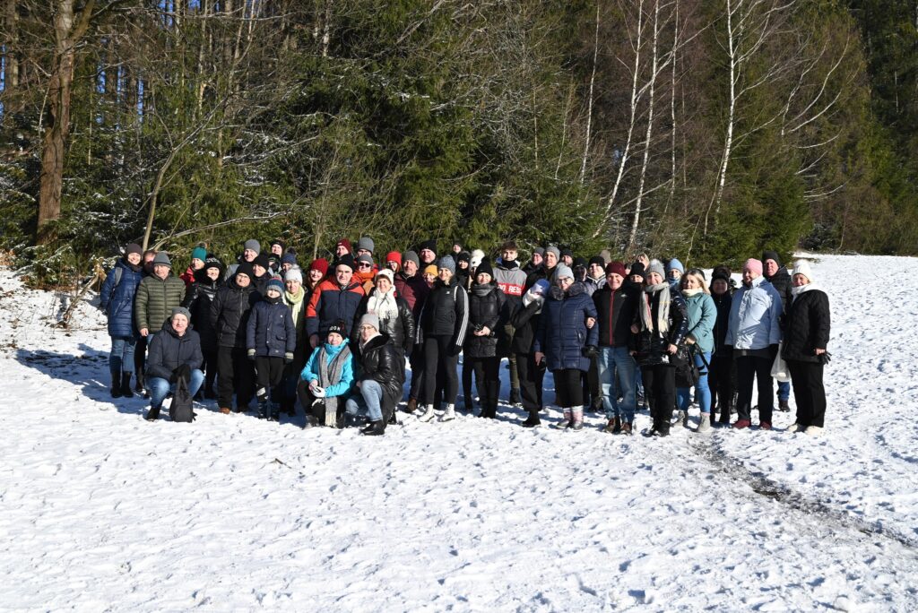 Zdjęcie przedstawia grupę pięćdziesięciopięcio osobową pozującą do zdjęcia grupowego na polanie w zimowej scenerii, podczas kuligu w Istebnej.