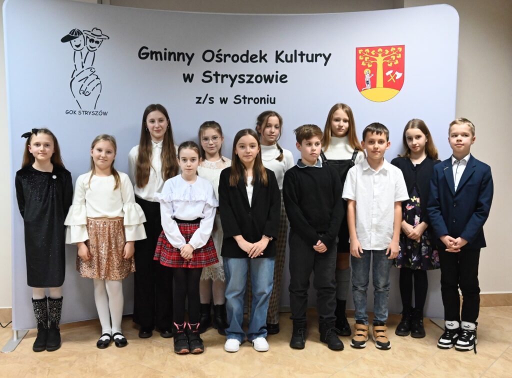 Dwanaście pozujących do zdjęcia osób, trzech chłopców i dziewięć dziewczynek z klas 4-6, podczas konkursu muzycznego „Kolęda i Pastorałka”.