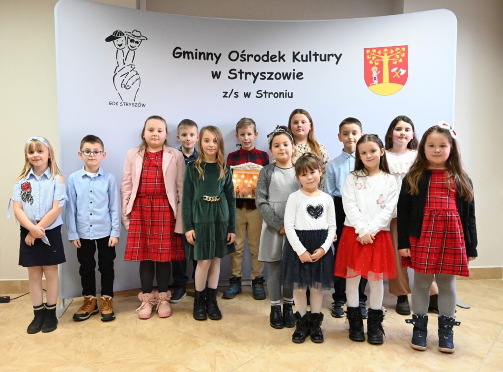 Trzynaście pozujących do zdjęcia osób, czterech chłopców i dziewięć dziewczynek z klas 1-3, podczas konkursu muzycznego „Kolęda i Pastorałka”.