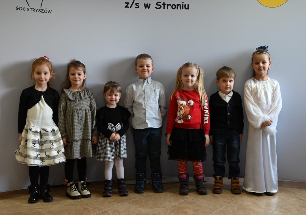 Siedem pozujących do zdjęcia osób, dwóch chłopców i pięć dziewczynek z kategorii „Przedszkolaki”, podczas konkursu muzycznego „Kolęda i Pastorałka”.