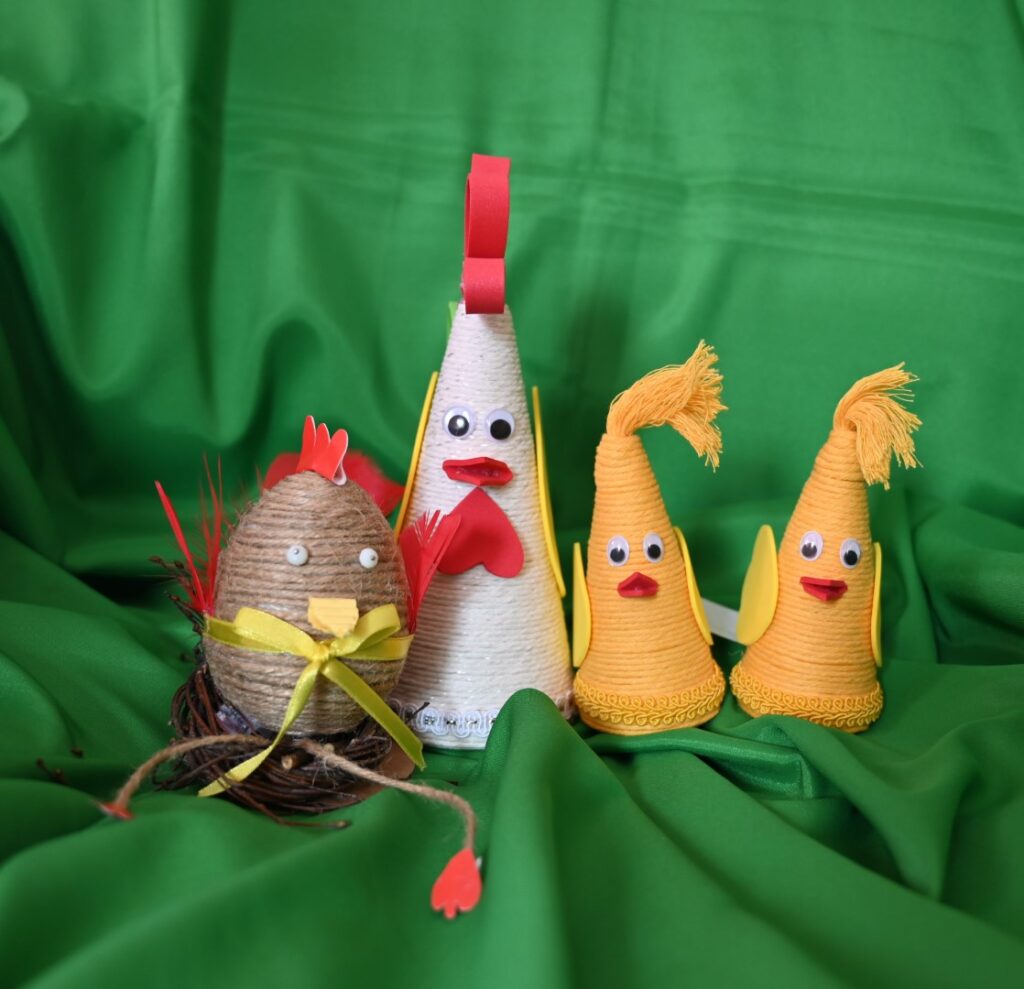 prace plastyczne z konkursu „Wielkanocna Pisanka”. Trzy pisanki w kształcie jednego większego białego i dwóch żółtych małych stożków przedstawiają kury natomiast czwarta z nich jest w kształcie jajka, w kolorze brązowym i przedstawia kurę z wiszącymi nogami