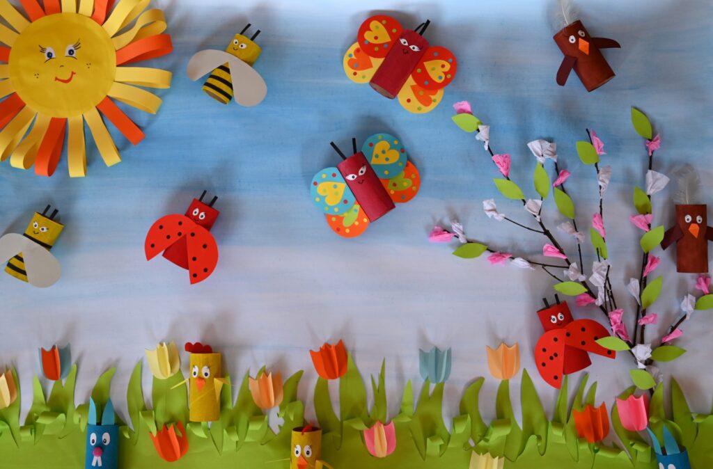 Praca plastyczna z konkursu „Pierwszy Dzień Wiosny”a na niej znajdują się zajączki, motylki i słońce wykonane z papieru, na tle wiosennego tła.