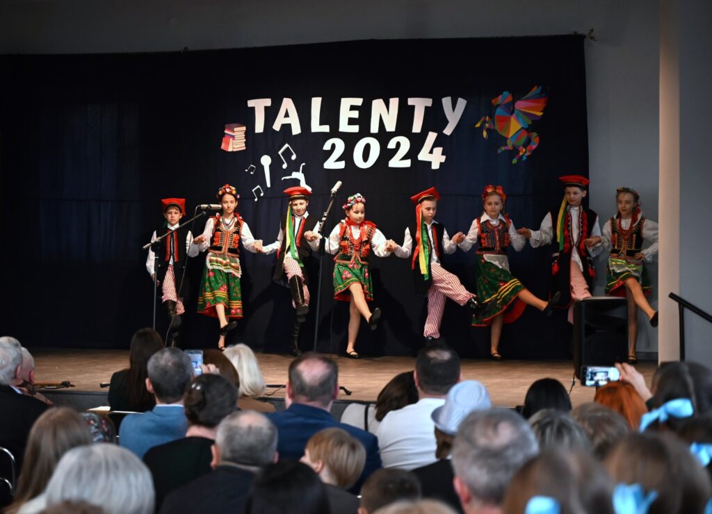 podczas Międzyszkolnego Talent Show 2024 w Domu Strażaka w Łękawicy na scenie tańczy grupa czterech dziewczynek i czterech chłopców z Zespołu Szkolno – Przedszkolnego ze Stronia. Mają na sobie tradycyjne stroje krakowskie